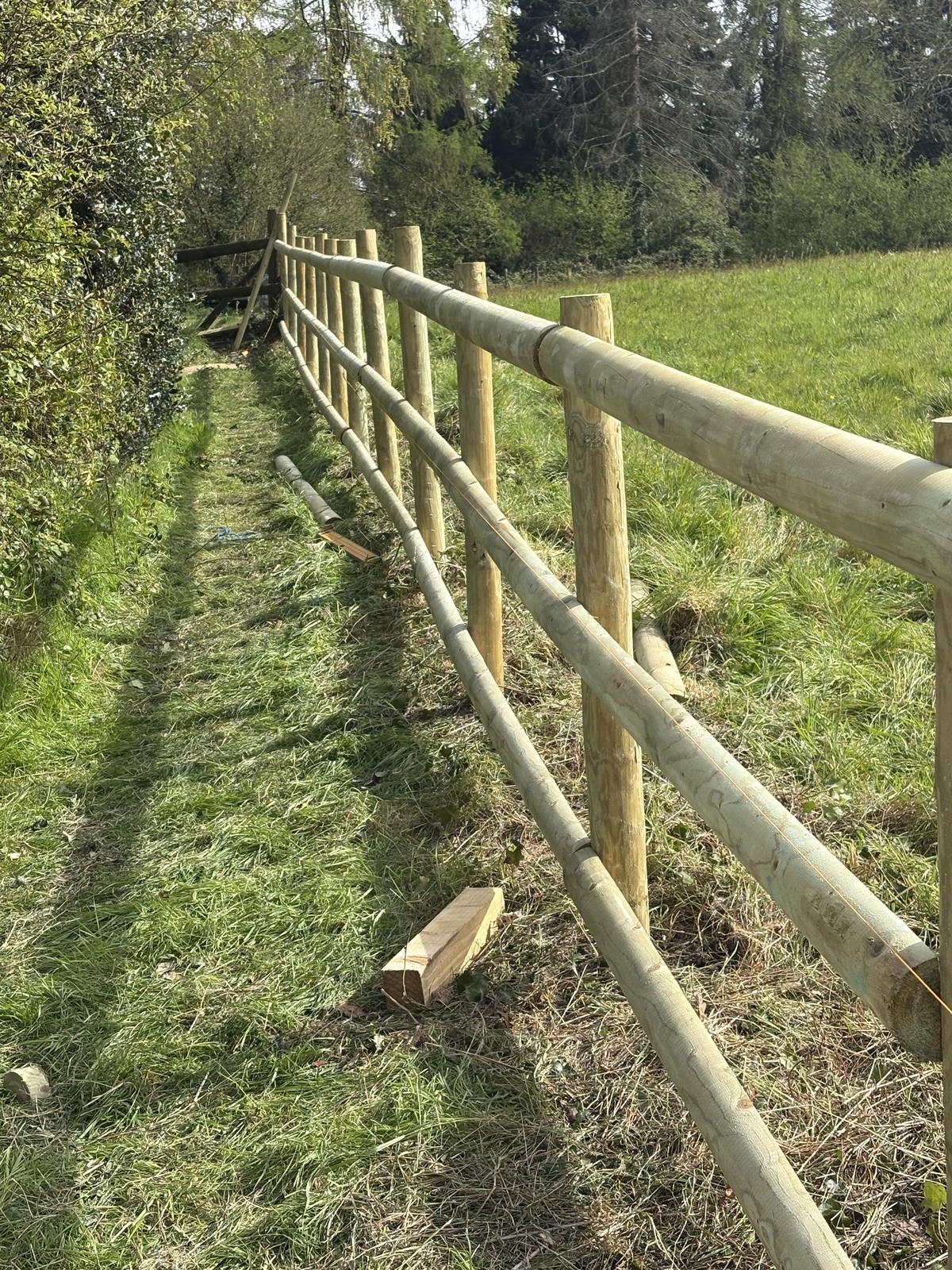 New round post and rail fence beside a field