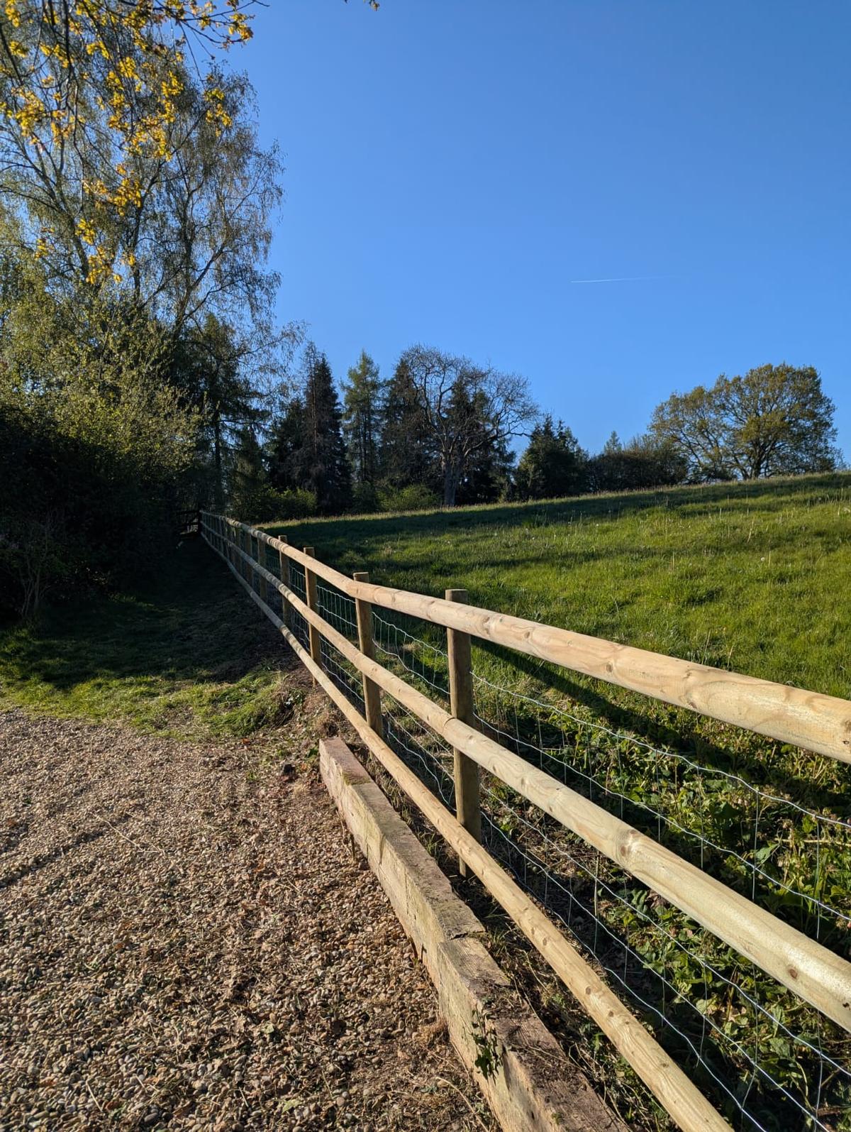 Post and rail fence with stock mesh running up a sunny field