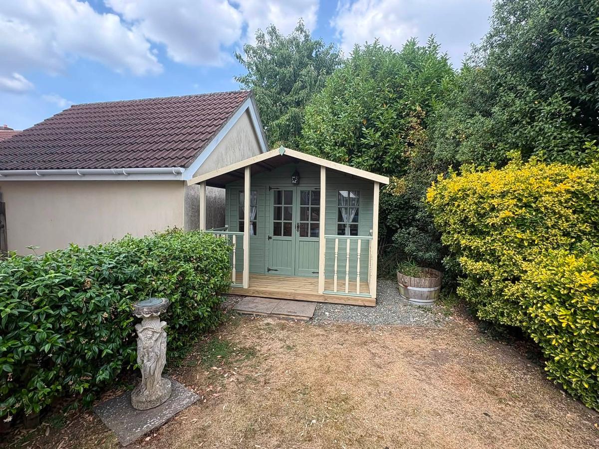 Restored summerhouse in sage green set among shrubs